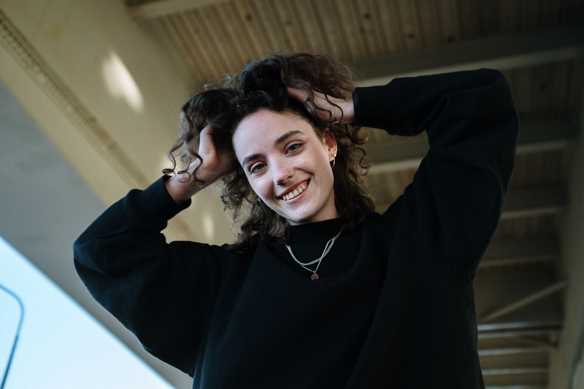 Portrait of a smiling woman outdoors in an urban setting, wearing a black sweatshirt.